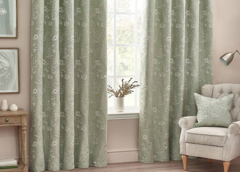 Woven eyelet curtains a jacquard floral design in a calming blue shade, hung in a room with green walls and a white ceiling.