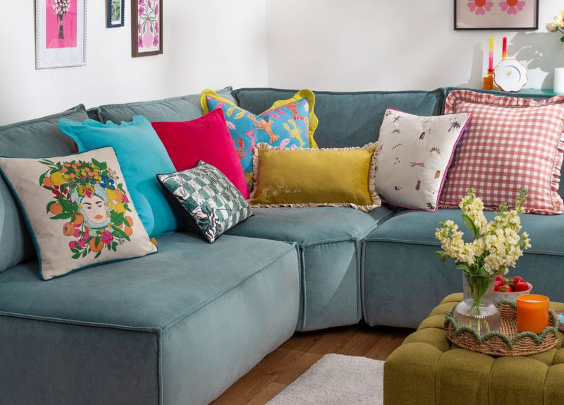 An arrangement of sofa cushions of various colours and designs, displayed on a muted blue sofa.