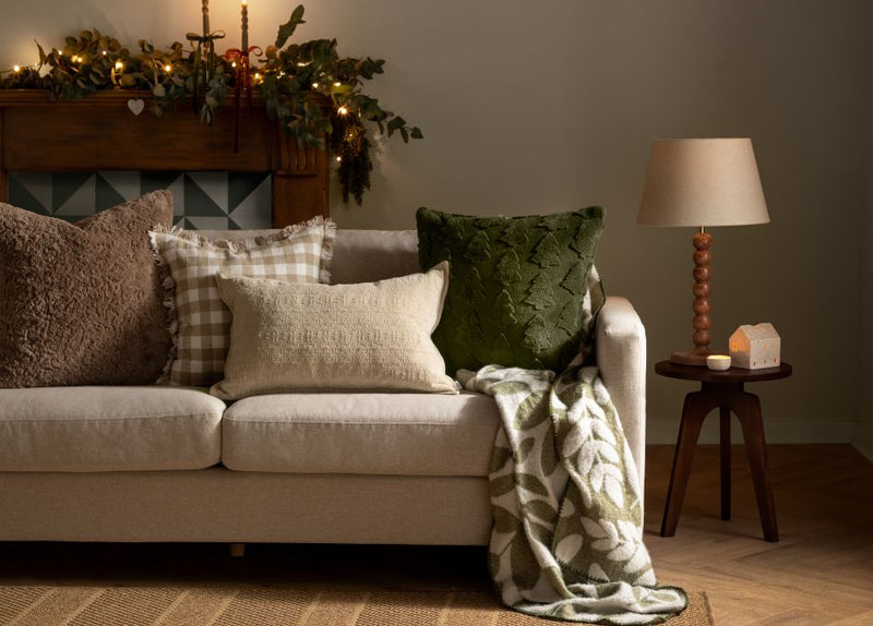 A festive sofa with Christmas cushions, a garland and candle sticks scattered along the back on the mantle piece