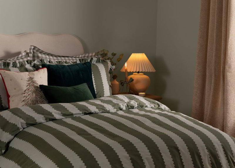 A bedroom with Christmas cushions and a green and light blue striped duvet cover.