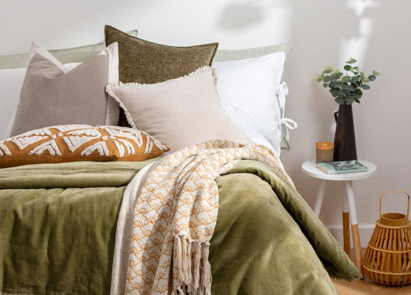 scandi style bed decor with neutral cushions and olive green throw on bed