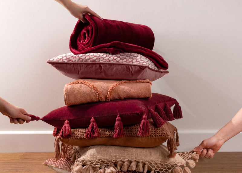 a pile of cushions in red, pink and beige tones.