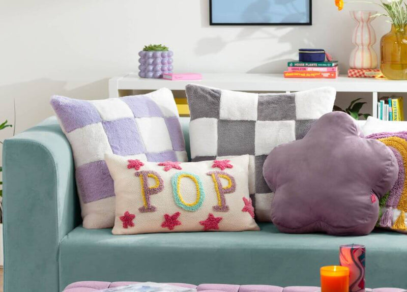 An arrangement of sofa cushions of various colours and designs, displayed on a muted blue sofa.