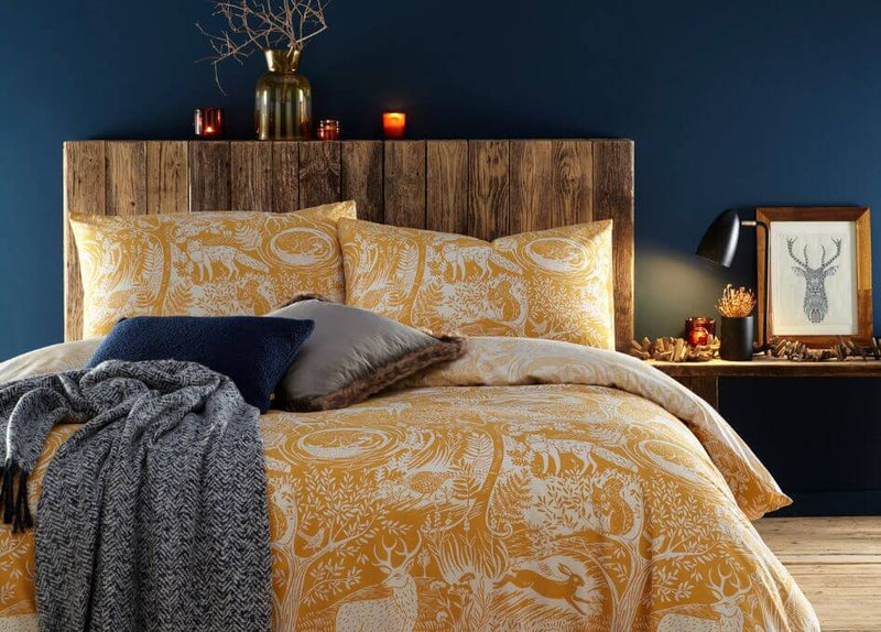 A winter bedroom with navy walls, winter foliage and a yellow duvet cover set with a printed design of winter woodlands and animals.