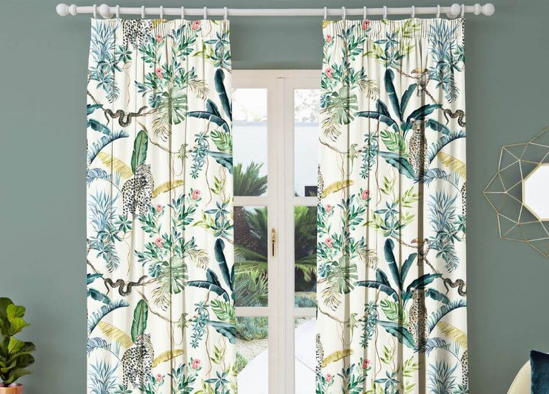 A closeup image of emerald green curtains with a jacquard geometric design, opened to reveal a white window sill overlooking an outdoor scene.