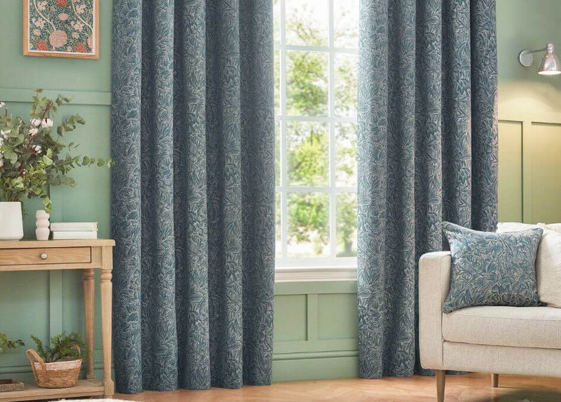 Woven eyelet curtains a jacquard floral design in a calming blue shade, hung in a room with green walls and a white ceiling.