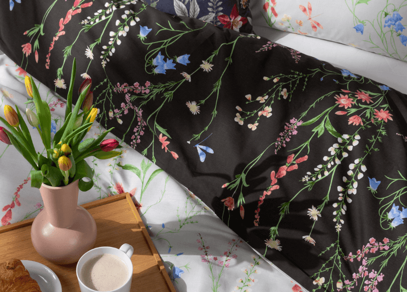 Interior gifts for mum, including a vibrant floral duvet set, a vase of flowers and a serving tray holding breakfast foods.