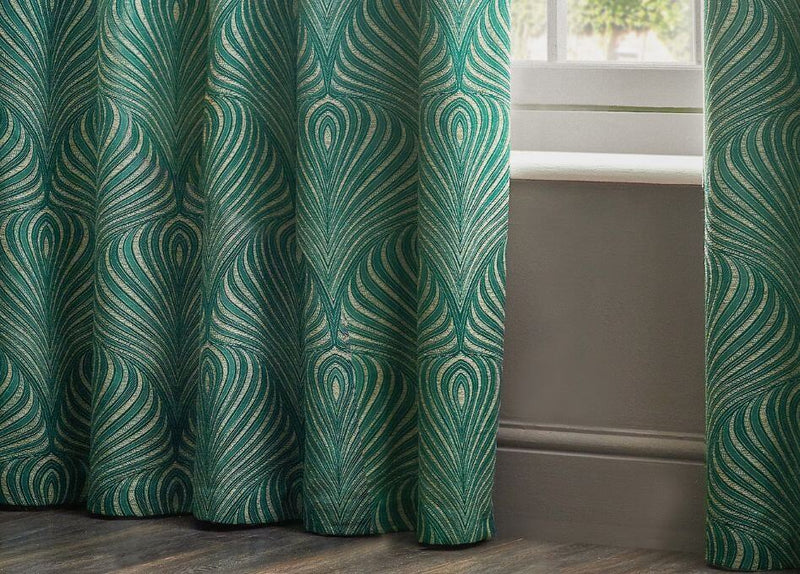 A closeup image of emerald green curtains with a jacquard geometric design, opened to reveal a white window sill overlooking an outdoor scene.