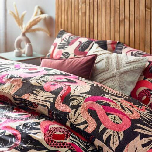 A black and ruby pink duvet cover set with a tropical design of snakes and leaves, arranged on a bed with coordinating scatter cushions.