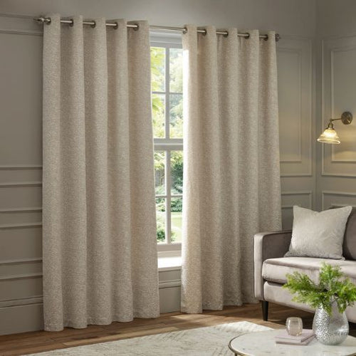 A pair of ivory white curtains for the living room, next to a cream coloured sofa with a cream textured cushion on top