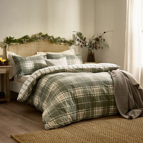A soft brushed cotton duvet cover set in a check design in green and neutral hues. With festive garland across the top of the bed and a soft grey throw on the bottom.