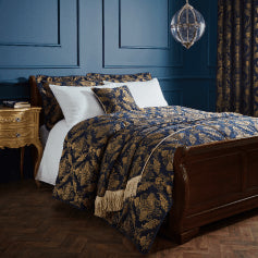 A luxury navy bedspread with a gold jacquard design of elegant florals, made on a bed with matching pillow shams and plain white bedding.