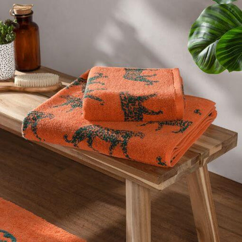 Two orange towels of varying sizes with jacquard leopard designs, folded and displayed on a wooden bench.