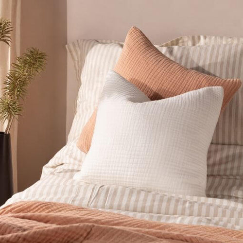 White and pink crinkle cotton bed cushions, placed one in front of the other on a bed with a striped duvet cover set and a matching crinkle cotton throw.