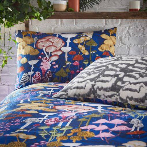 A bright blue bedding set with a multicoloured fungi design, made on a bed and revealing a monochrome reverse design.