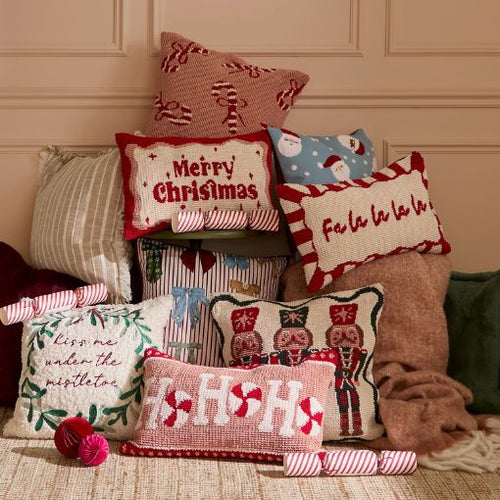A collection of christmas and festive cushions piled up on each other in a range of festive pinks and reds, with phrases "merry christmas" and "fa la la la la" on them