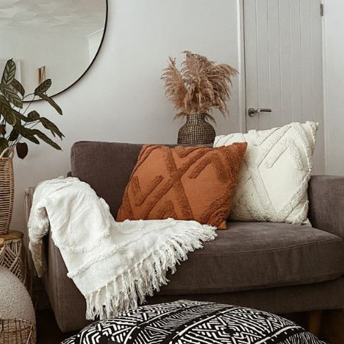 Two sofa cushions with geometric tufted cotton designs, arranged on a neutral sofa.