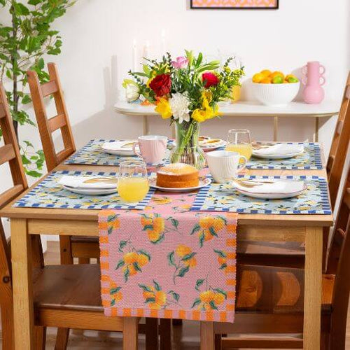 A dining table decorated with table linen, including a table runner and a set of four placemats with coordinating fruit designs.