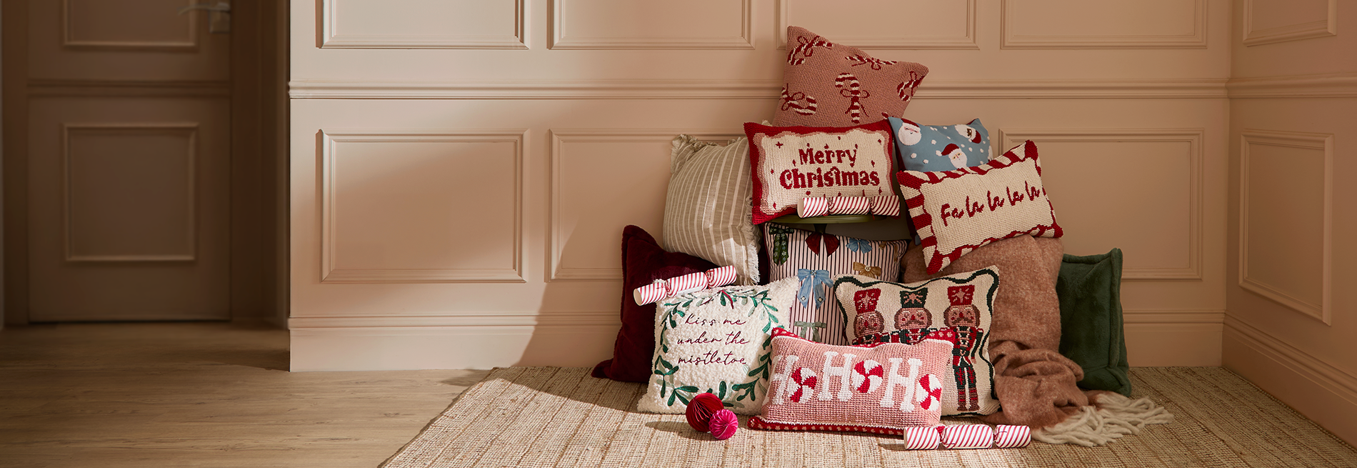 Decorative Christmas pillows on a wooden floor against a beige wall.